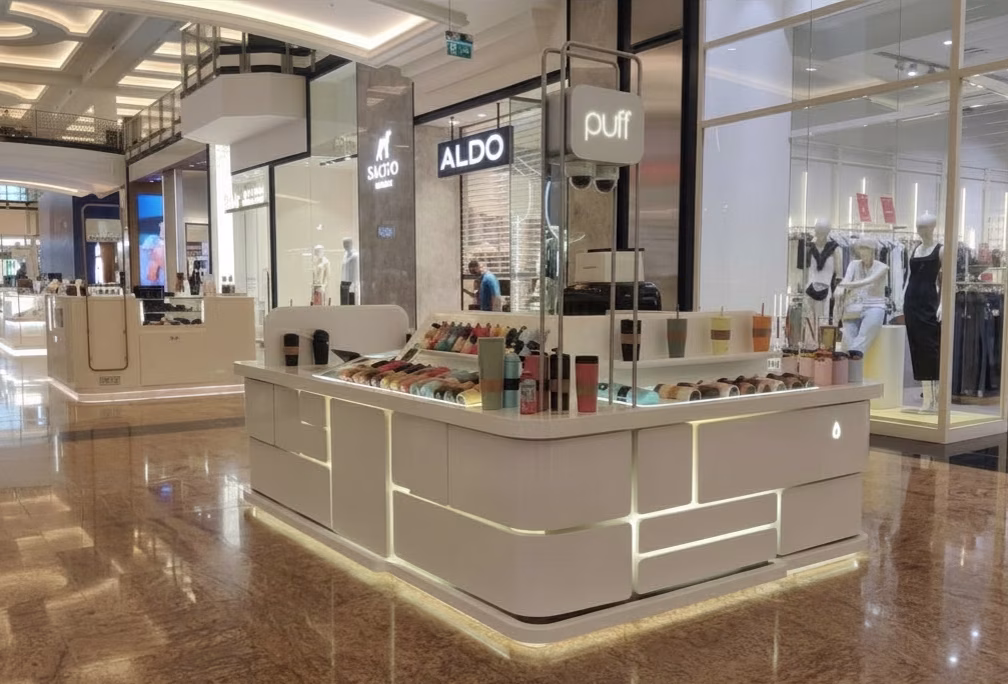 Curved mall kiosk with veneer cabinet body, illuminated display shelving, and stainless steel pylon signage