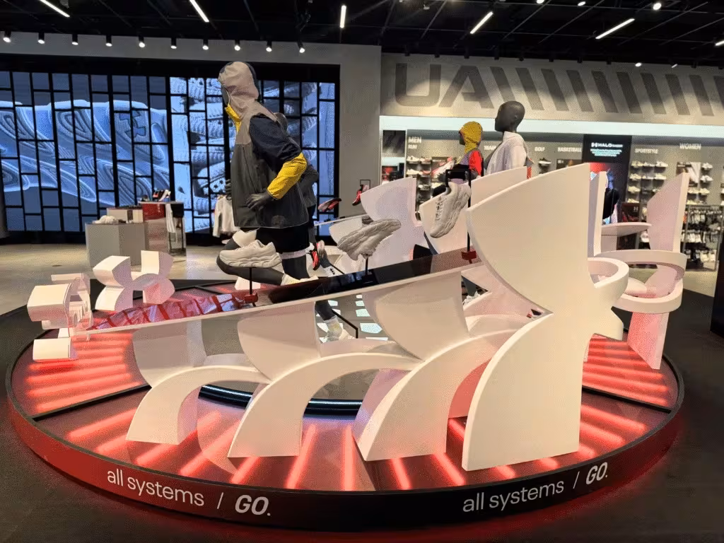 Best POS Display in Dubai: Under Armour Footwear Wall by New Royal Advertising LLC Store display with mannequins and shoes on platform.